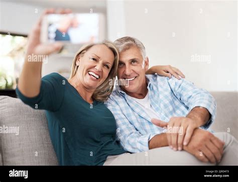 smile an affectionate mature couple taking selfies together while sitting on the sofa at home
