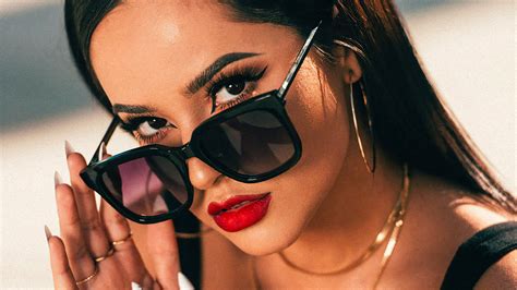 Becky G X Dime Is Holding Sunglasses On Nose And Black Dress With Gold
