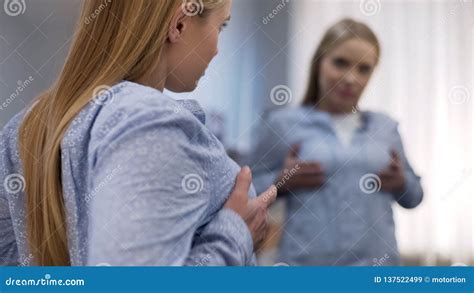 Young Female Touching Chest In Front Of Mirror Unsatisfied With Her Breast Size Stock Image