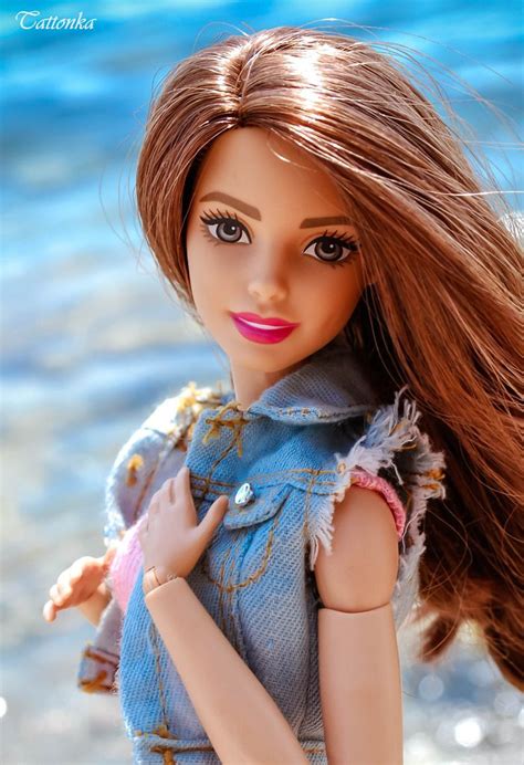 A Close Up Of A Barbie Doll With Long Hair And Blue Dress On The Beach
