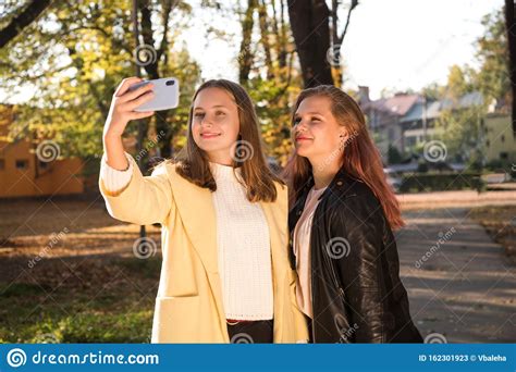 Two Beautiful Teen Girls Taking Selfie On The Phone While In Sunny Autumn Park Stock Image