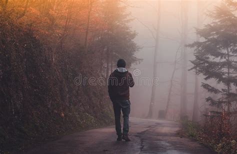 Man Walking Alone On A Road Through A Dark Foggy Forest Stock Image