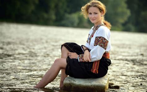 A Girl Sits On A Rock Near The Water In Traditional Dress