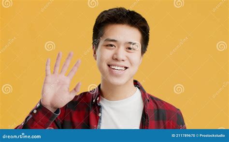 Joyful Asian Man Waving Hello Posing Standing On Yellow Background