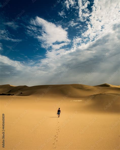 Back View Of A Man Walking Alone In The Desert Under A Dramatic Cloudy