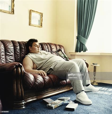 Young Man Lies Slouched On A Sofa Watching Videos And Holding A Packet
