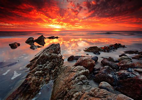 Photo Of Rock Formation In Body Of Water Against The Sun With Clouds Hd