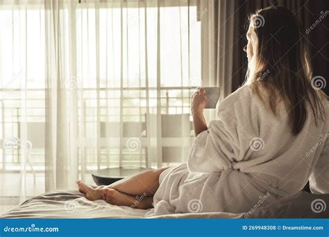 Woman In White Bathrobe Lying On Sofa And Relaxing With Cup Of Tea At