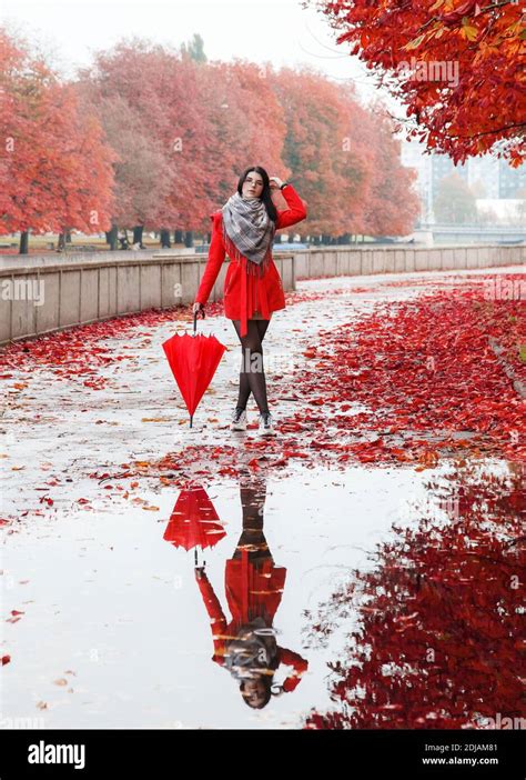 Young Girl In A Red Coat With An Umbrella Stands On The Alley Of The