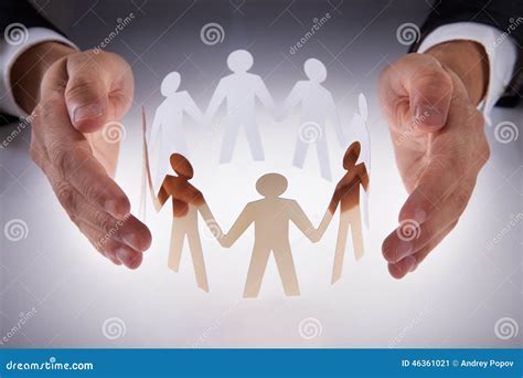 Businessmans Hands Protecting Team Of Paper People On Desk Stock Photo