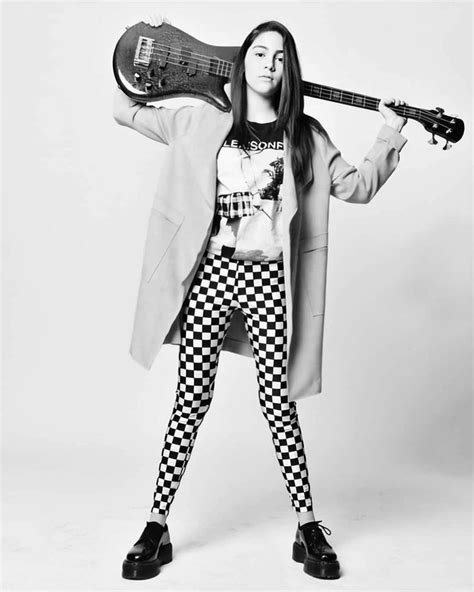a woman in checkered leggings holding an electric guitar over her head while standing against a