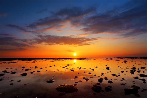 Wide Photography Of A Bodies Of Water With Rocks And Sunset Background