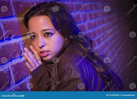 Frightened Pretty Young Woman Against Brick Wall At Night Stock Photo