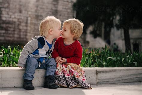 Two Small Children Sitting On A Low Wall Share A Kiss By Julia Forsman