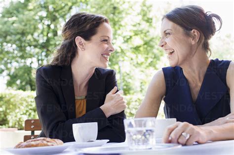 Two Mature Female Friends Chatting Over Coffee In Garden Stock Photo