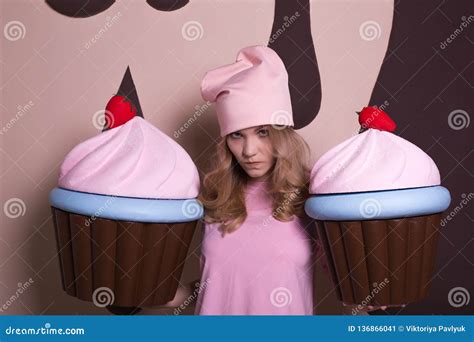 Upset Blonde Woman Wearing Pink Cap Holding Big Cupcakes At Studio