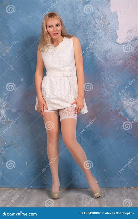 Blonde Long Legged Model In White Minidress And White Stockings Posing