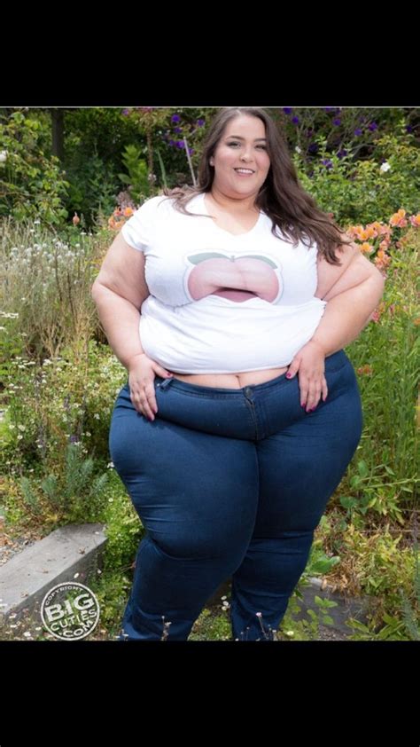 A Woman With Big Belly Standing In Front Of Some Flowers And Plants Wearing Blue Jeans