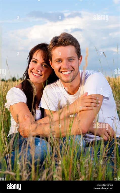 Happy Couple Sitting On A Meadow Or Grainfield In Summer Embracing Each