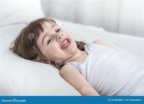 Cute Little Girl Smiling While Lying In A Cozy White Bed Stock Image
