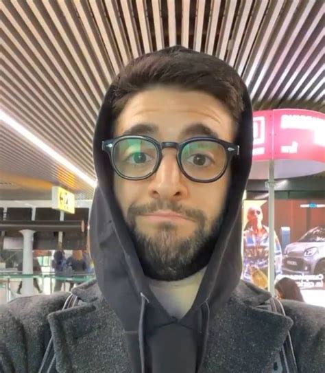 A Man Wearing Glasses And A Hoodie In An Airport