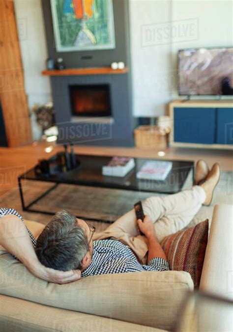 Man relaxing, watching TV on living room sofa - Stock Photo - Dissolve