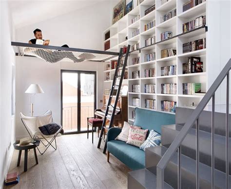 A Man Sitting On Top Of A Ladder In A Living Room Next To A Bookshelf