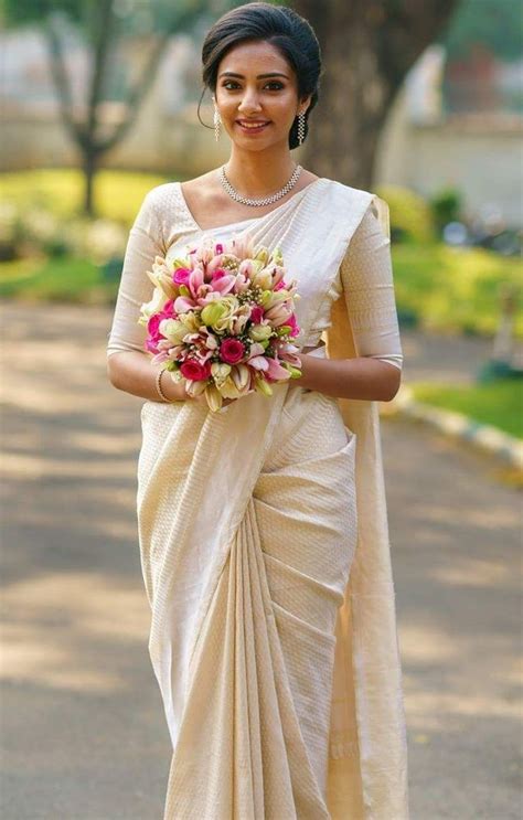 a woman in a white sari holding a bouquet of flowers on her left hand