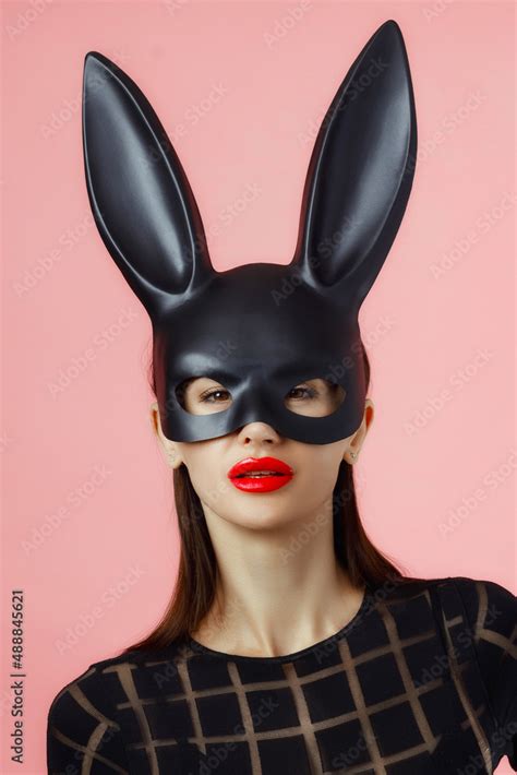sexy woman wearing a black mask easter bunny standing on a pink background and looks very
