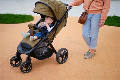 Woman Mother Walks With Toddler Baby Boy Sitting In A Stroller On The P
