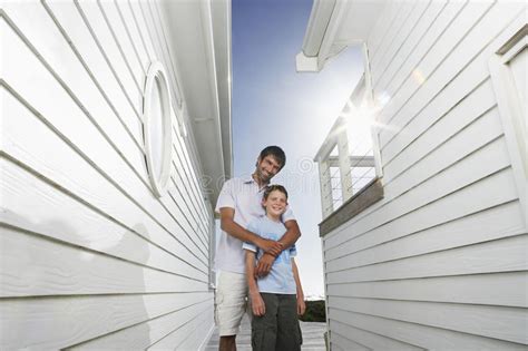 Father Standing Arm Around Son In Narrow Passageway Between Houses