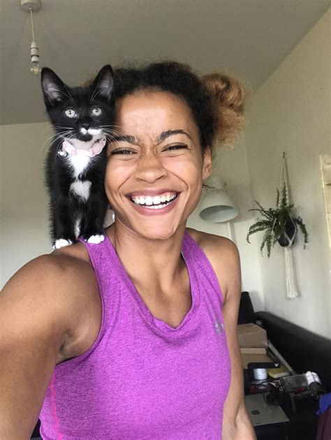 A Woman Holding A Black And White Cat On Her Shoulders While Smiling At