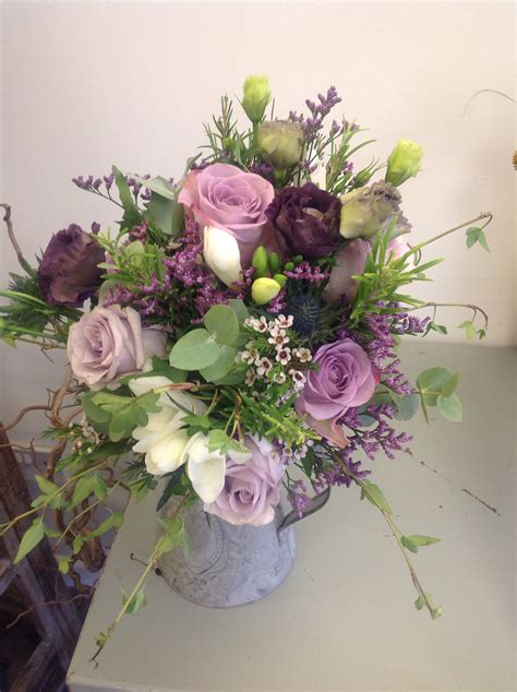 A Vase Filled With Lots Of Purple Flowers On Top Of A White Table Next
