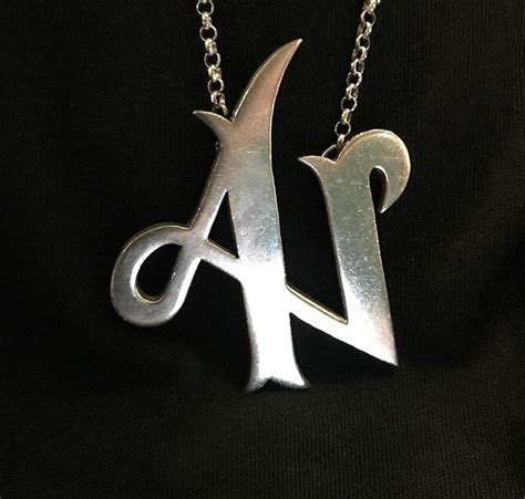 A Silver Necklace With A Pair Of Scissors On Its Side And The Letter A