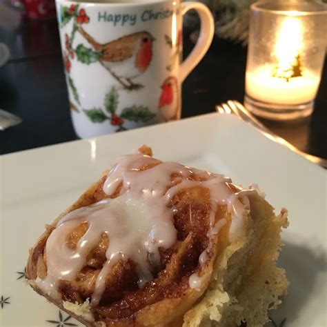 A Cinnamon Roll With Icing Sitting On A Plate Next To A Cup And Candle