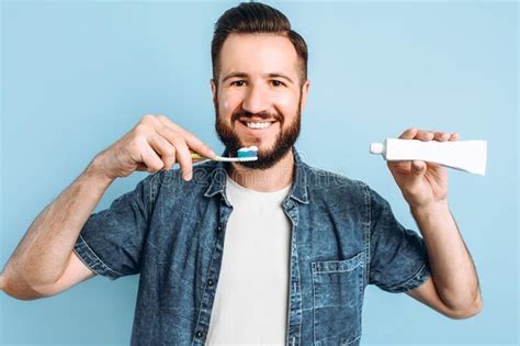 A Young Handsome Man With A Beard Is Brushing His Teeth On An Isolated