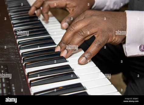 Fingers of an old African American man playing a keyboard piano wearing