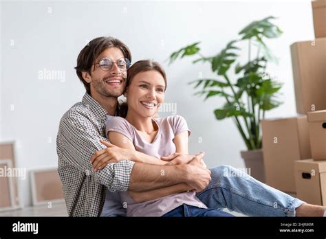 Smiling Millennial European Husband In Glasses Hugs Wife In Room