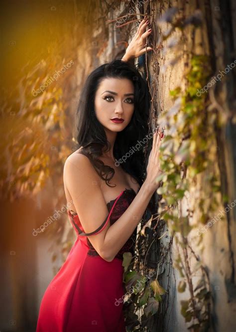 Красивая чувственная женщина в красном платье позирует в осеннем парке Молодая брюнетка мечтала