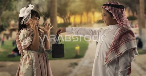 صبي وفتاه صغيران سعوديان مبتسمان ، الفتاه الصغيرة تضع يدها على خدها تشعر بالخجل يمسك الطفل