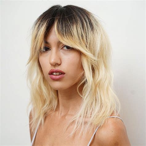 messy platinum blonde wavy textured lob with fringe curtain bangs and shadow roots the latest