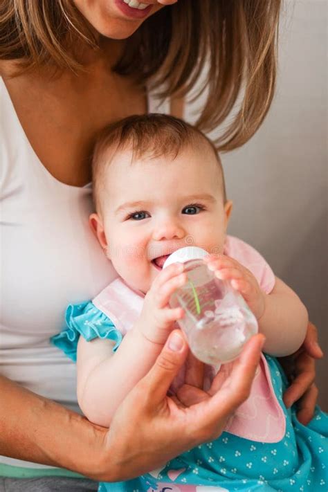 Adorable Little Caucasian Baby Girl Holds Bottle Of Water And Try To