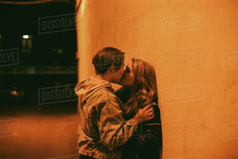 Lesbian Couple Kissing While Standing By The Wall In City At Night