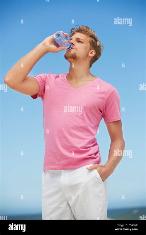 Young Man Drinking Water From A Water Bottle On The Beach Stock Photo