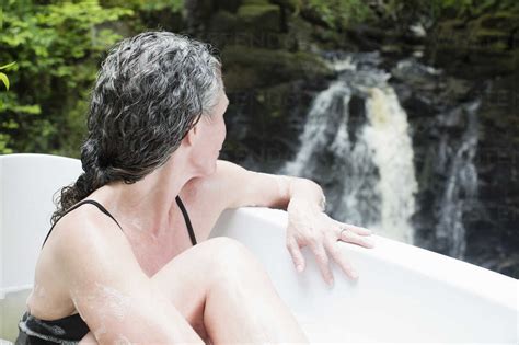 Mature Woman In Bubble Bath Gazing At Waterfall At Eco Retreat