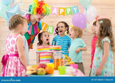 Group Of Children With Clown Blowing Candles On Cake At Birthday Party