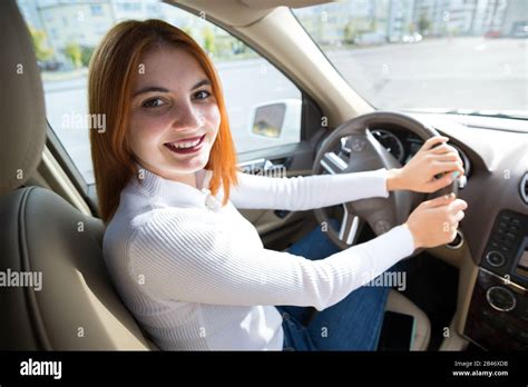 Young Redhead Woman Driver Behind A Wheel Driving A Car Smiling Happily