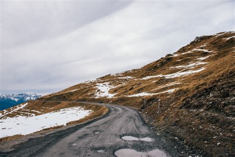 A Rough Mountain Road Curves Around A Wilderness With Patches Of Snow