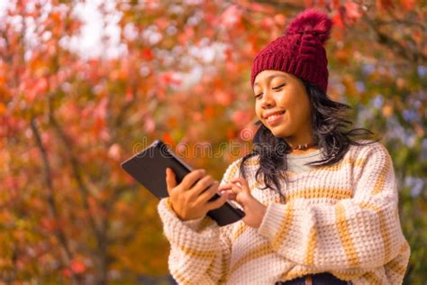 Closeup Shot Of A Happy Southeast Asian Girl Typing On Her Tablet Against The Red Trees Stock