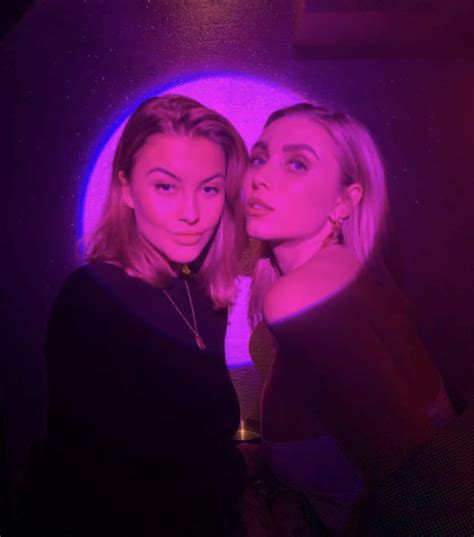 Two Beautiful Women Standing Next To Each Other In Front Of A Purple